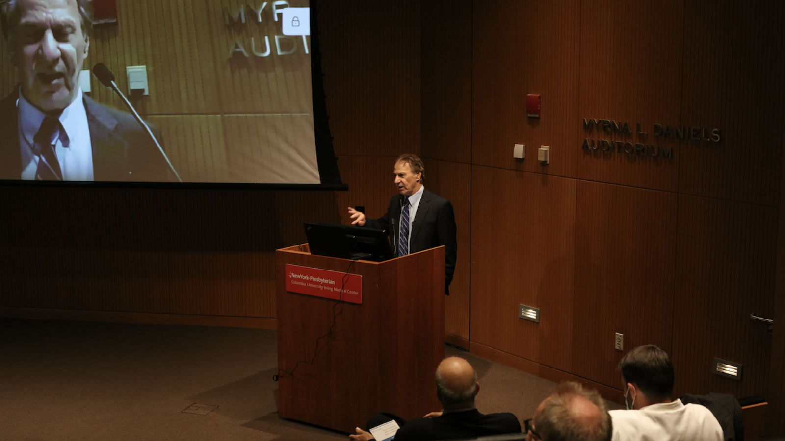 Man speaking at podium with slide show behind