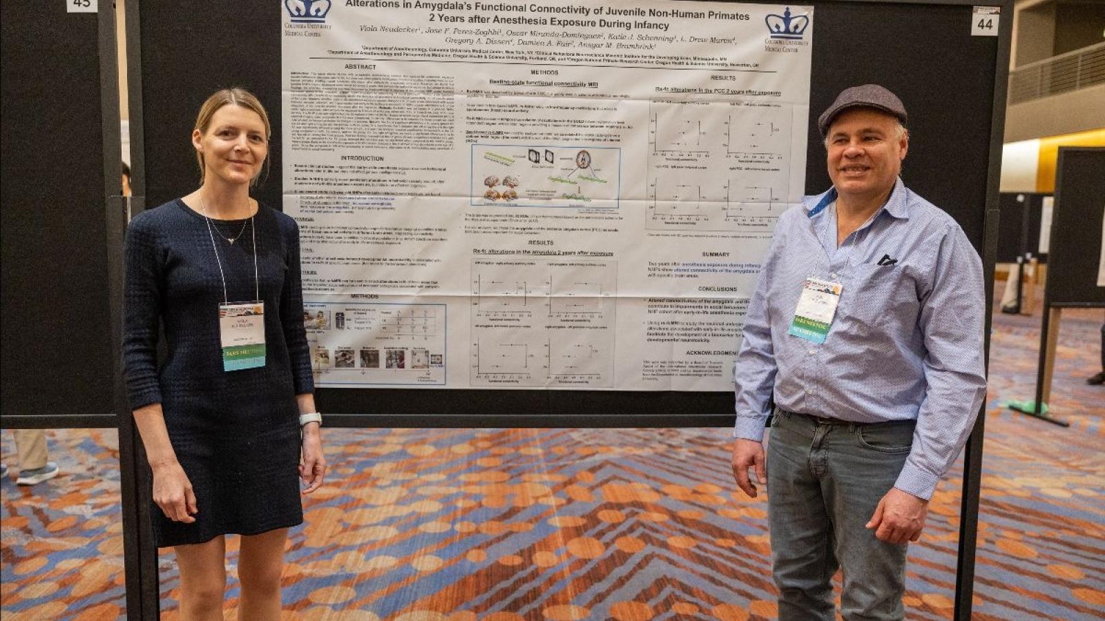 Two people standing in front of their poster at a conference