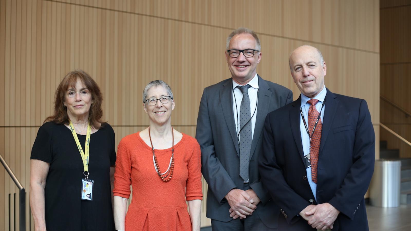 Four people in business dress stand in line, smiling at camera