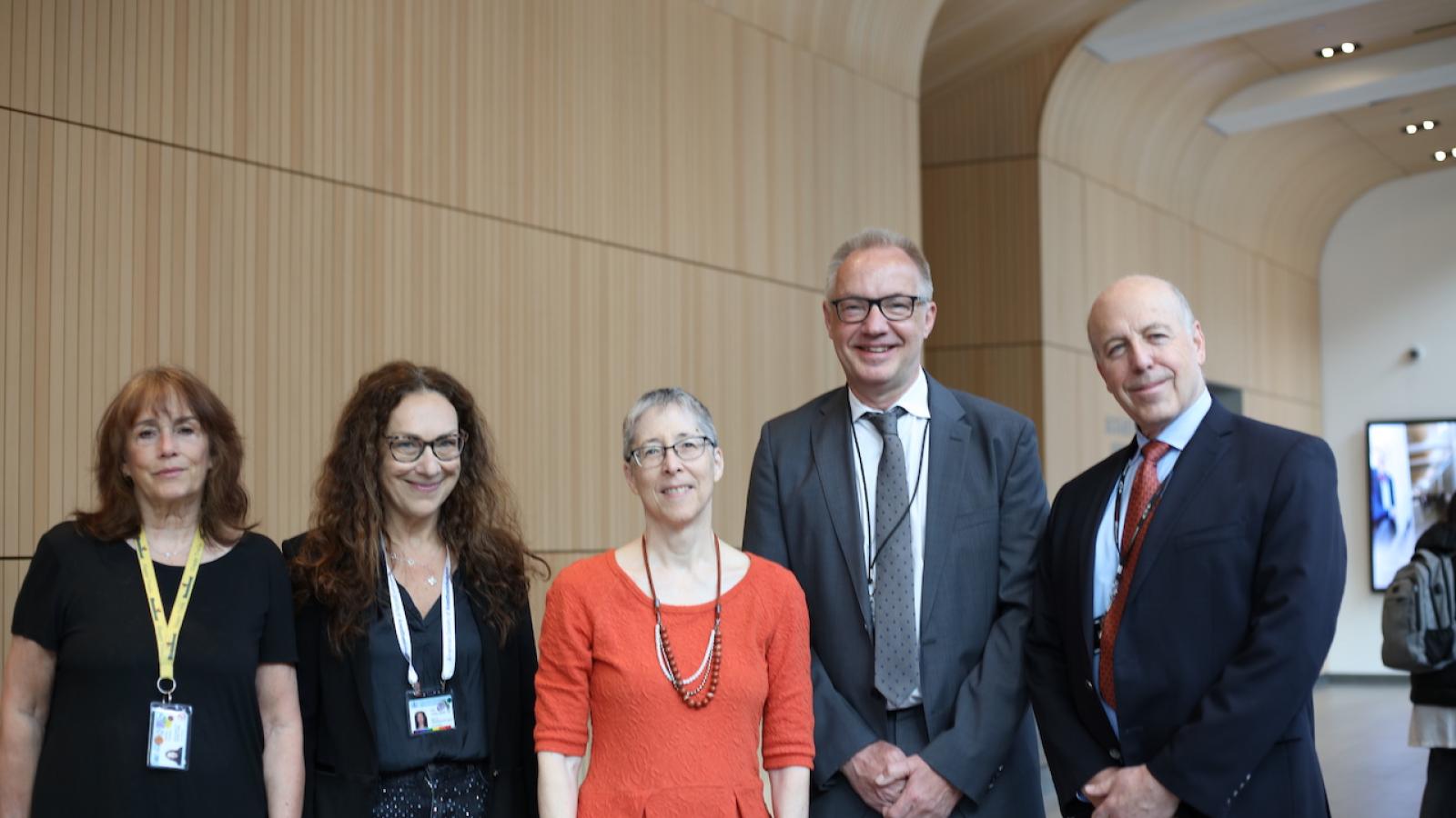 Five people in business dress stand in line, smiling at camera