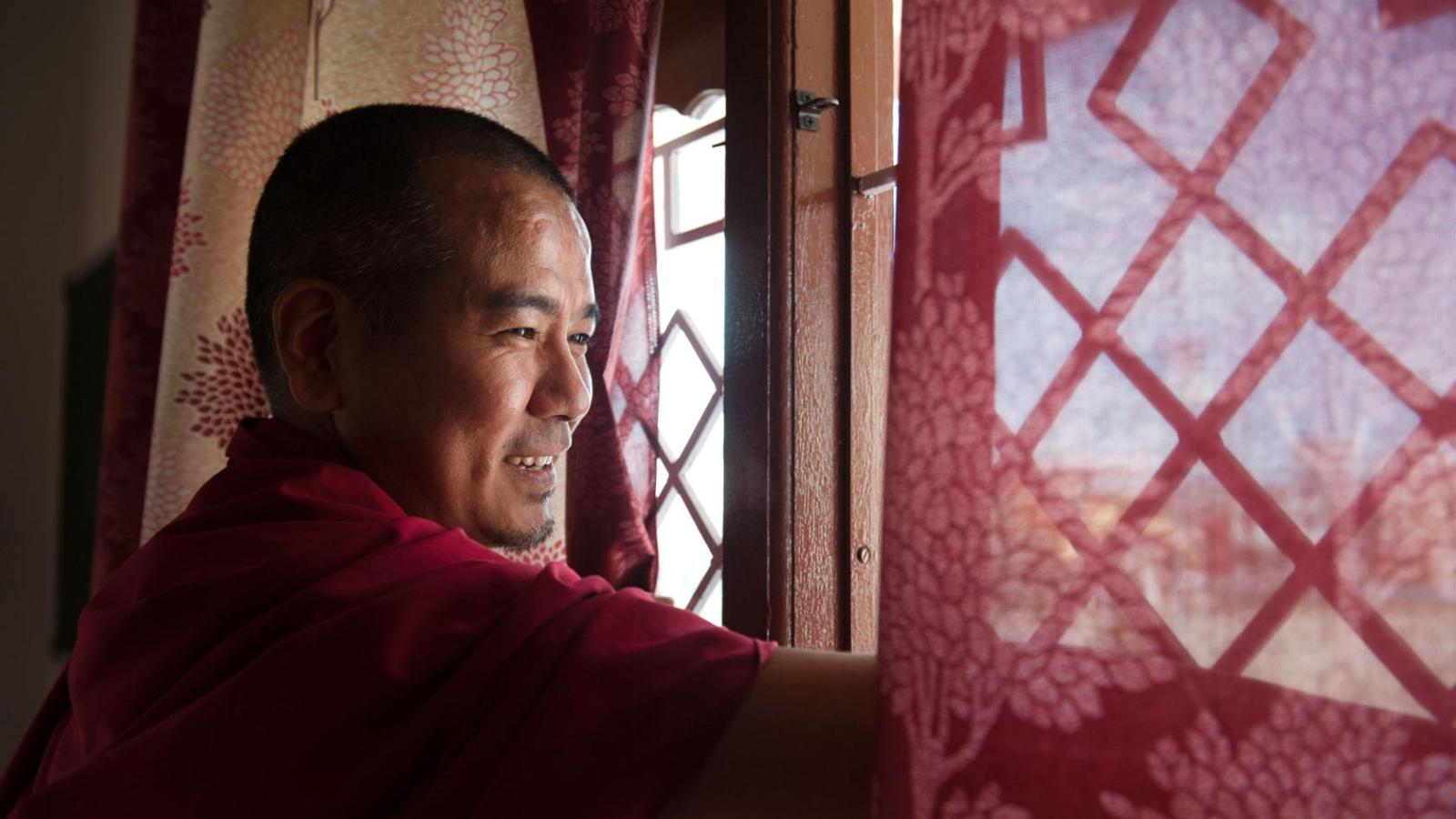 A senior monk looks out from a monastery window and watches junior monks during their morning debate in the courtyard. ©Nancy A Scherl 2019