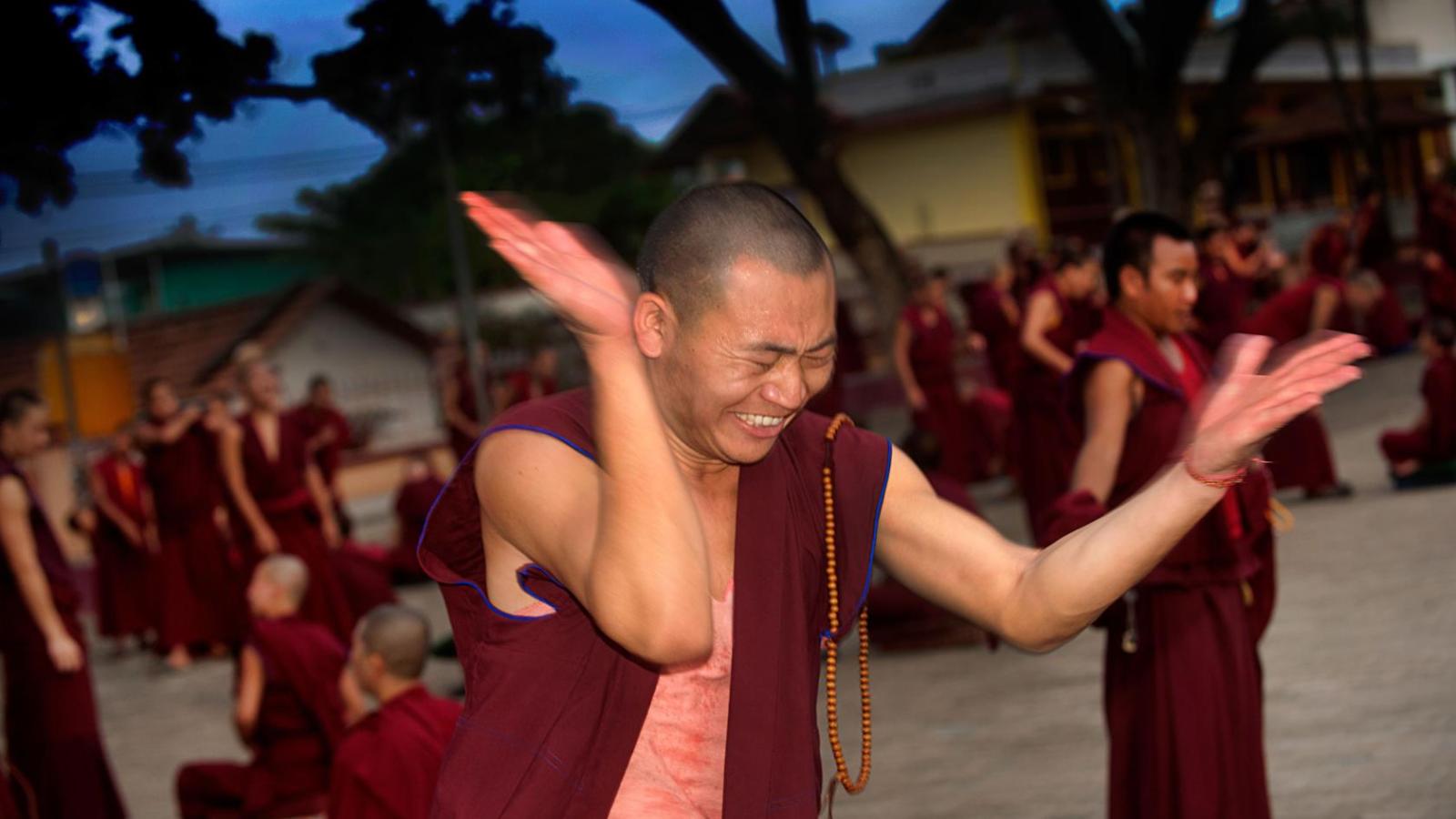 A monk uses the classic 'clap and hold' to emphasize a point during a debate where he is challenging a defender who is seated though out of frame.