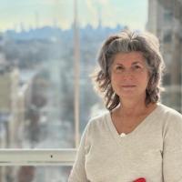 Woman standing in front of window, wearing white sweater and carrying red iPad folder
