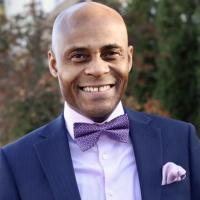 Man smiling, wearing lavender bowtie and shirt, blue jacket